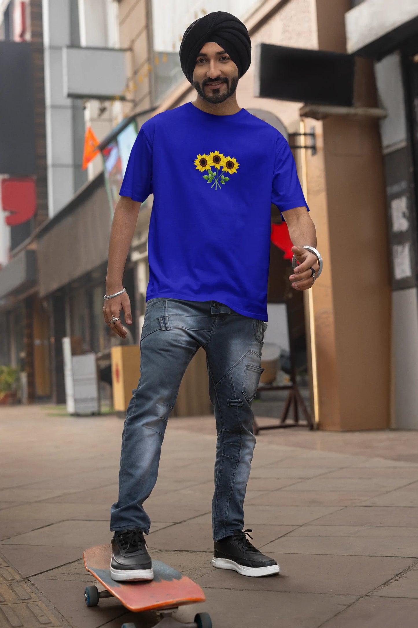 Second front view of a male model wearing a royal blue oversized t-shirt featuring three vibrant sunflowers arranged in a bunch. 