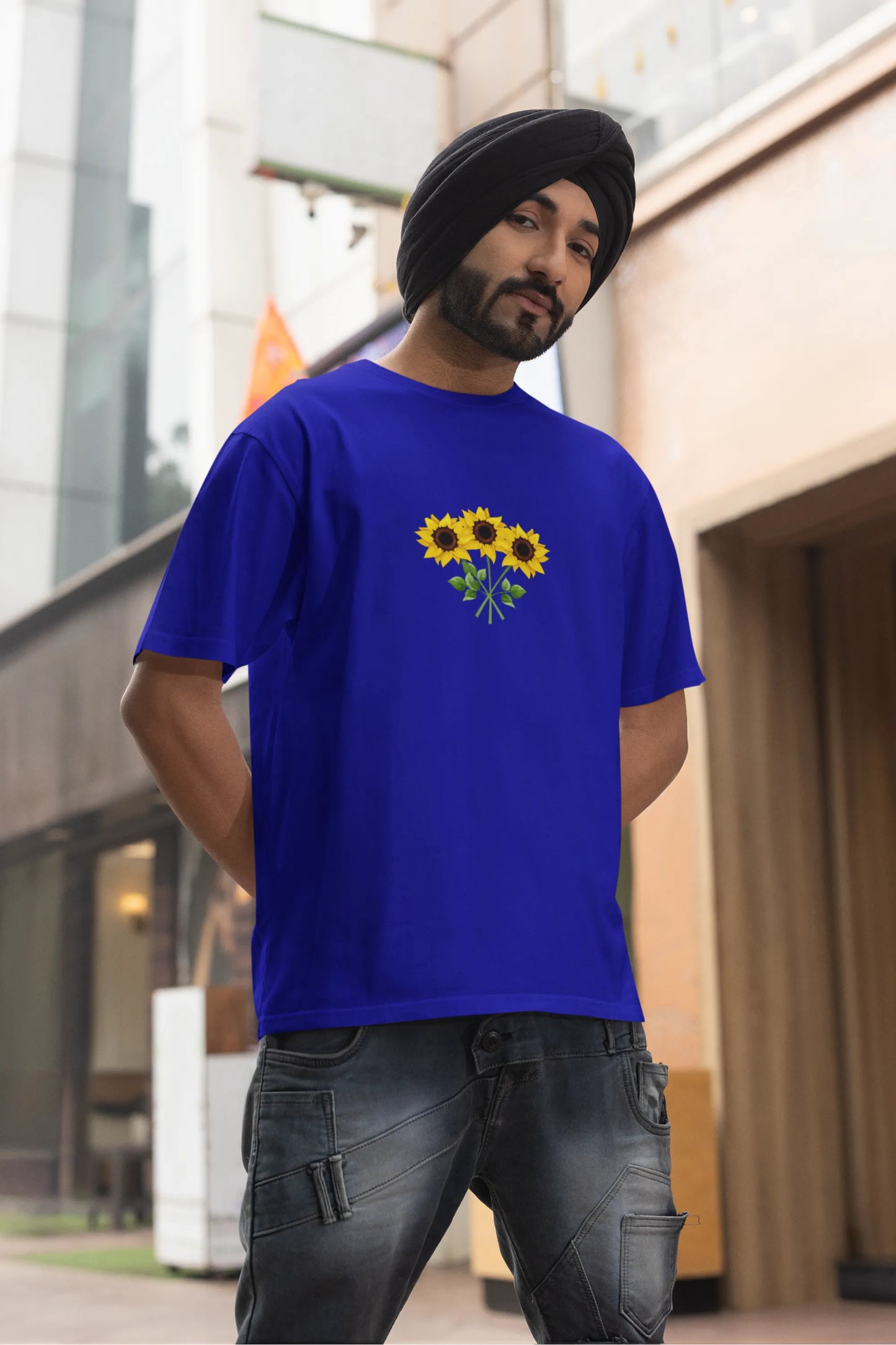 First front view of a male model wearing a royal blue oversized t-shirt featuring three vibrant sunflowers arranged in a bunch. 