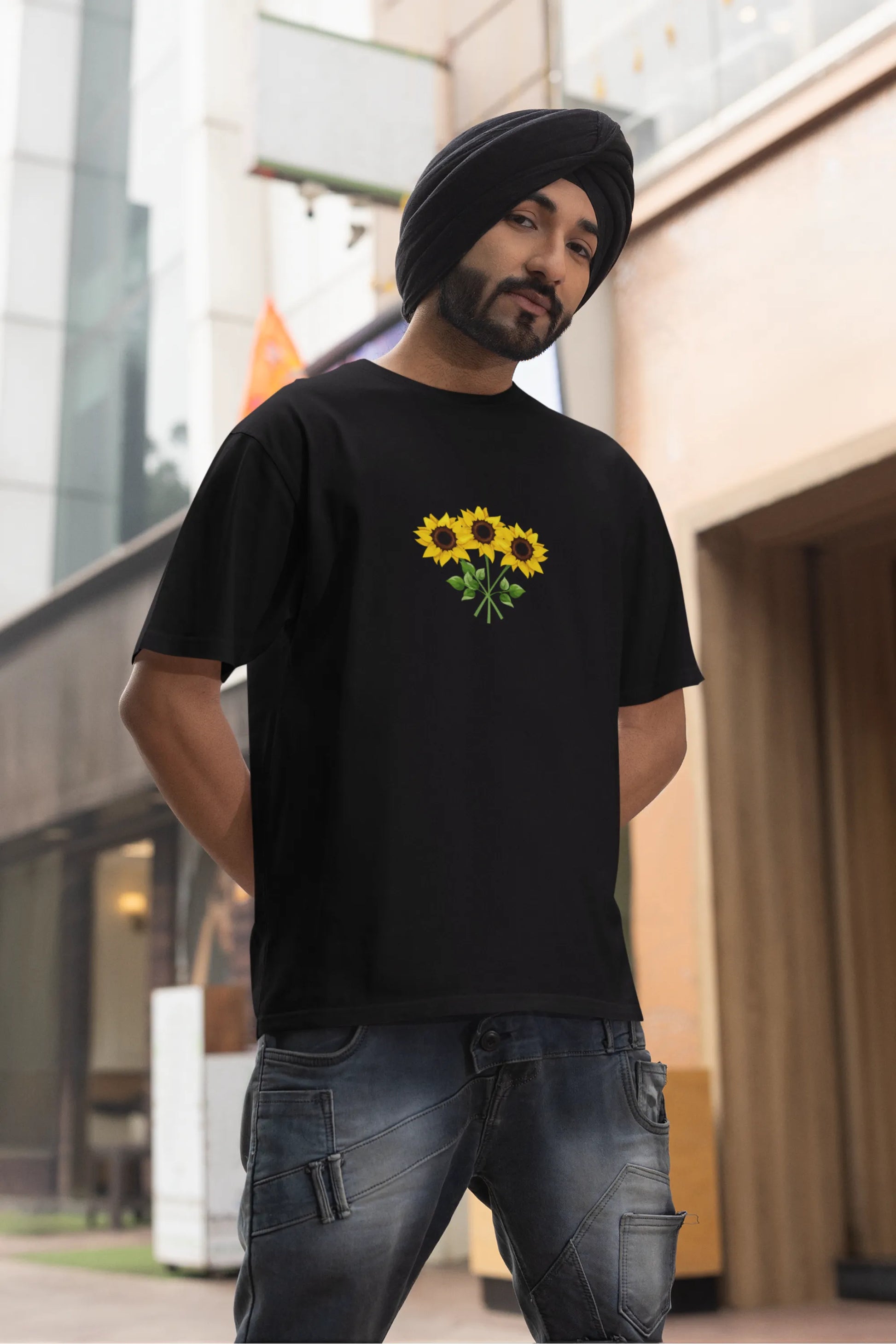 Third front view of a male model wearing a black oversized t-shirt featuring three vibrant sunflowers arranged in a bunch. 