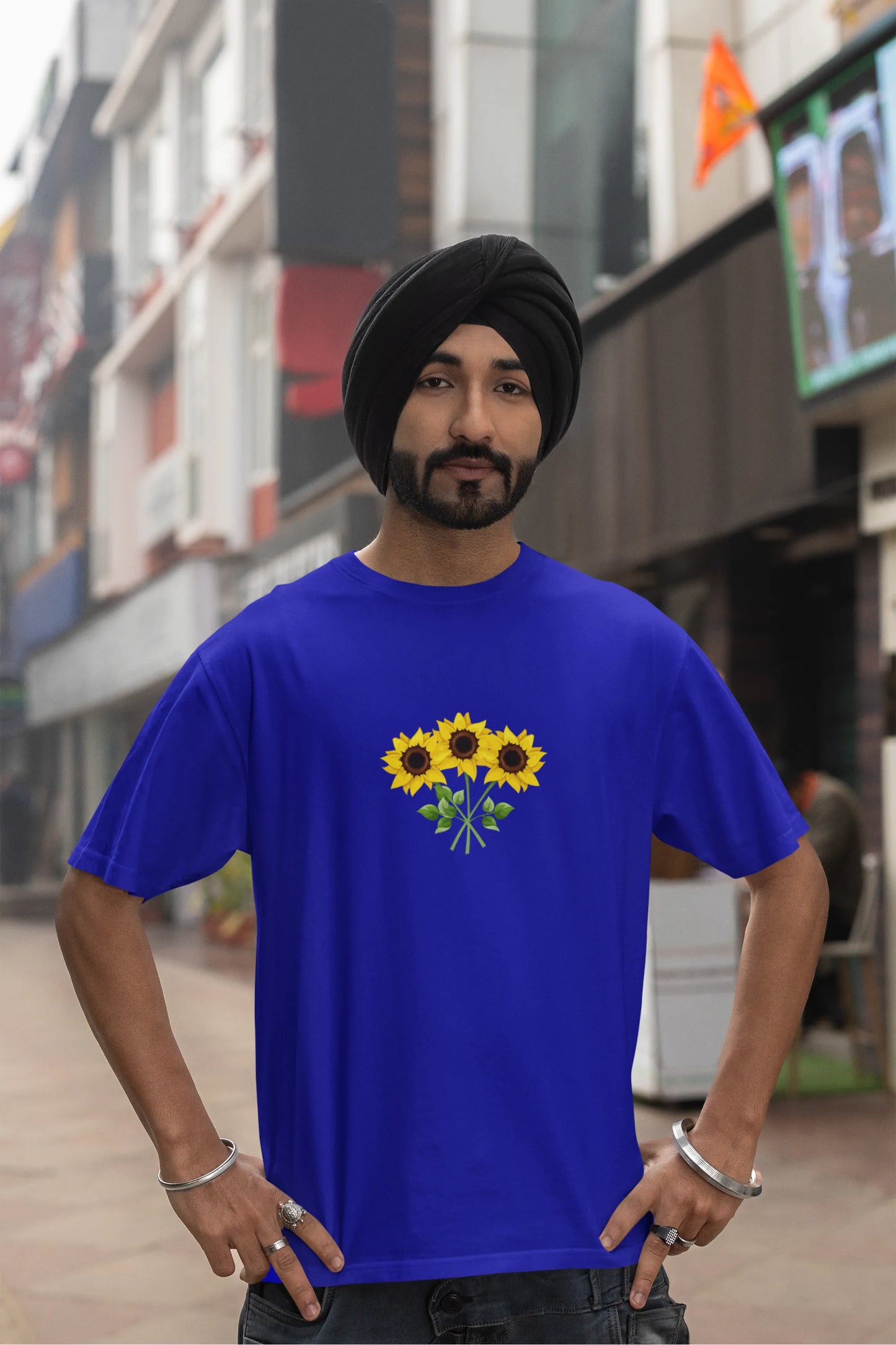 Fourth front view of a male model wearing a royal blue oversized t-shirt featuring three vibrant sunflowers arranged in a bunch. 