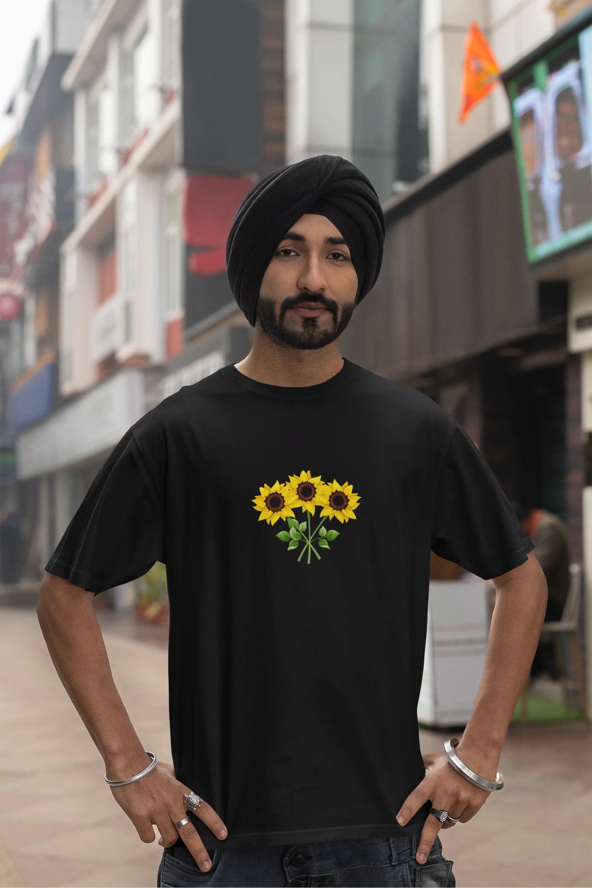 Fourth front view of a male model wearing a black oversized t-shirt featuring three vibrant sunflowers arranged in a bunch. 