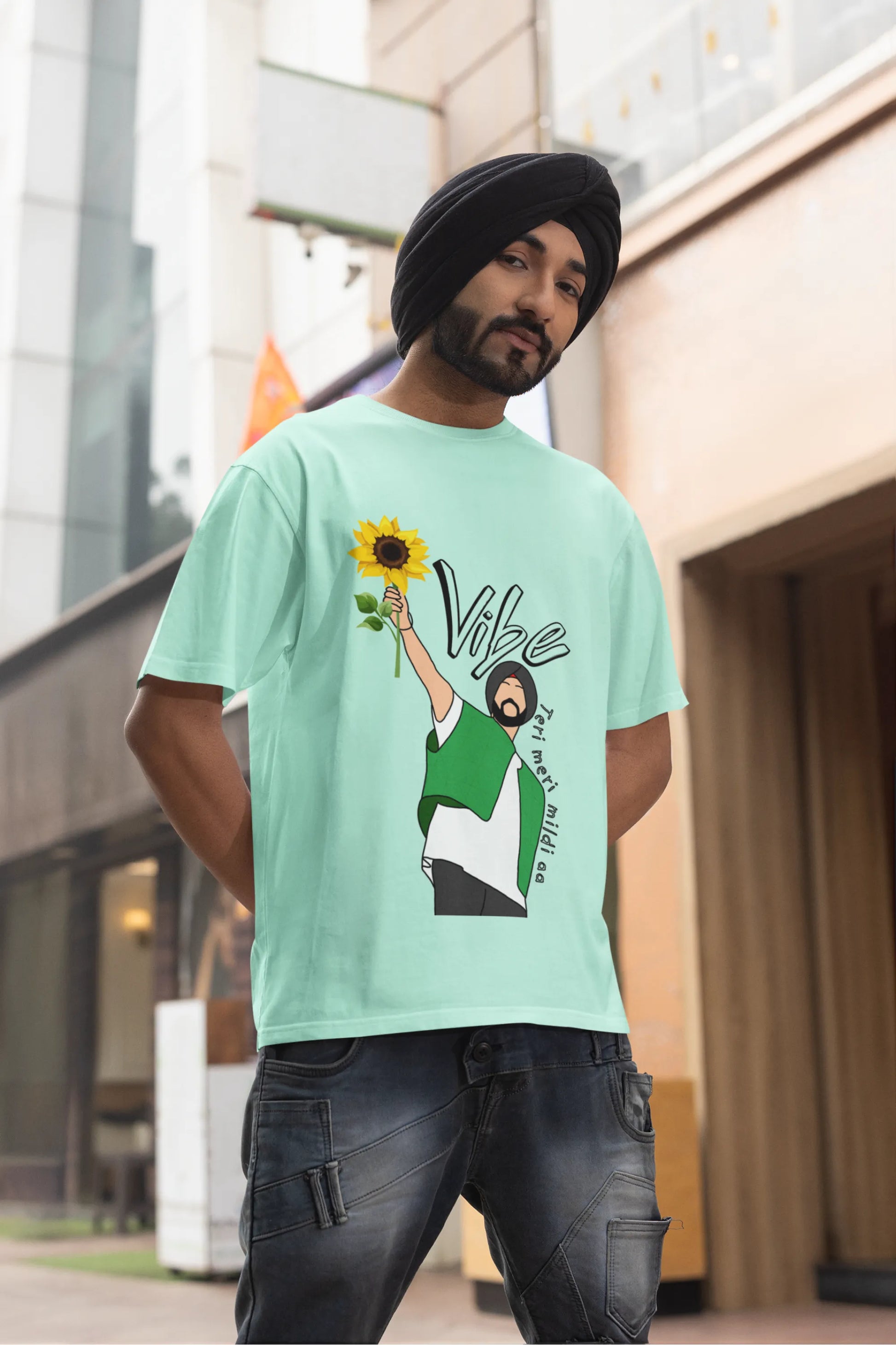 Second front view of male model wearing a mint green oversized t shirt with a design of Diljit Dosanjh holding a sunflower, with the text "Vibe Teri Meri".