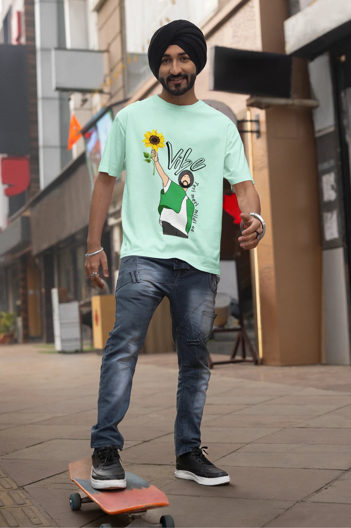 First front view of male model wearing a mint green oversized t shirt with a design of Diljit Dosanjh holding a sunflower, with the text "Vibe Teri Meri".