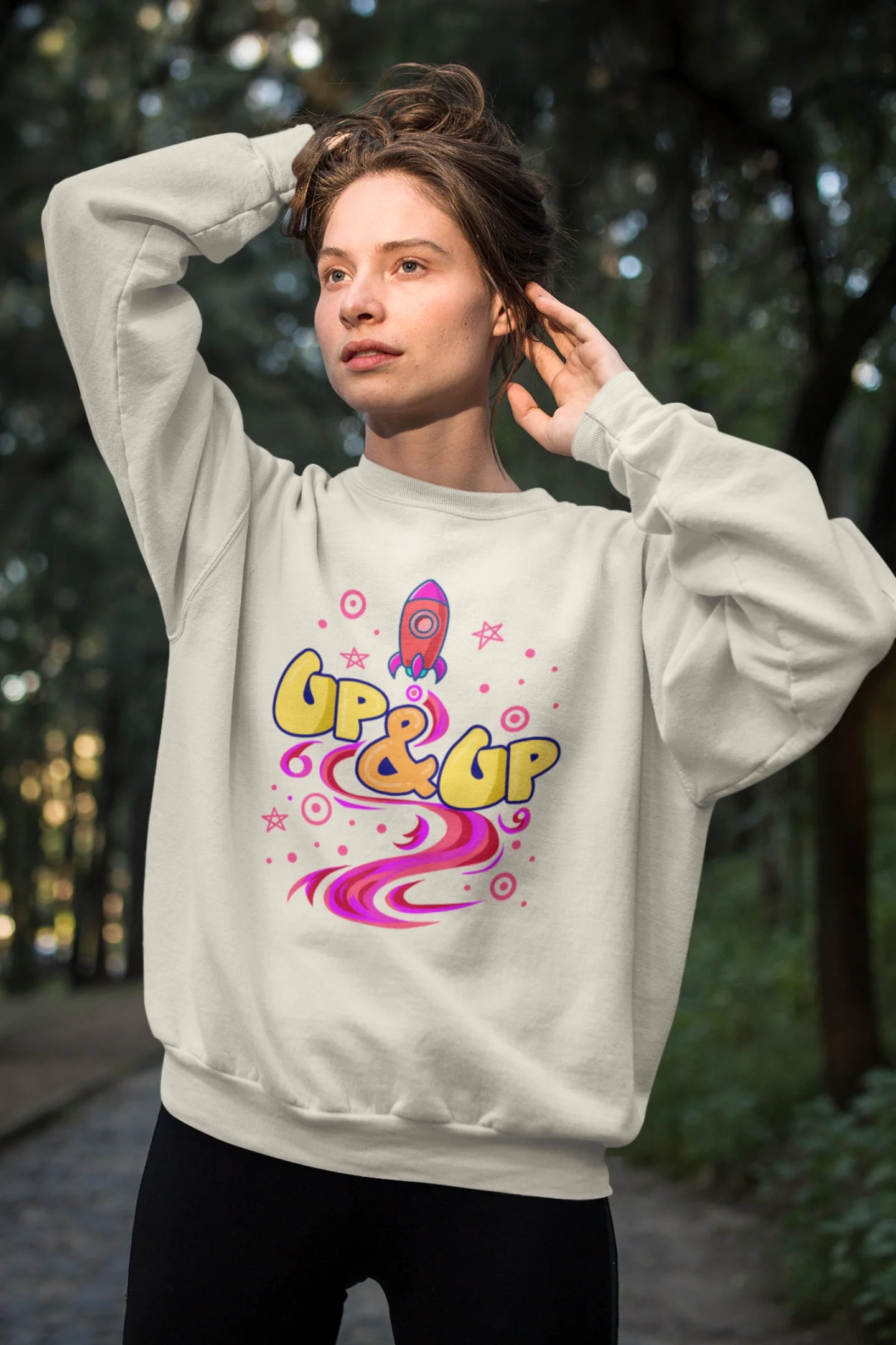 First front view of a female model wearing an cream sweatshirt with a rocket ship design and the text "Up & Up".