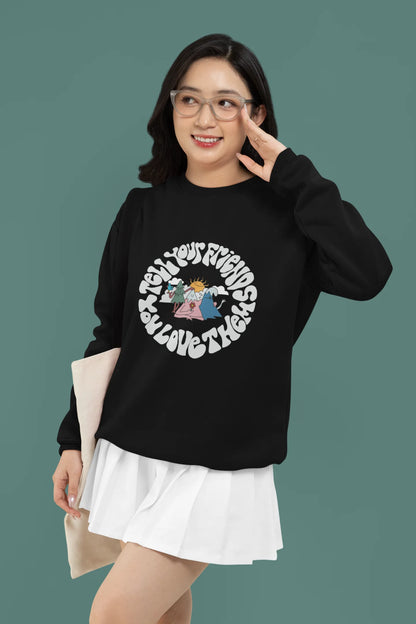 3rd front view of a female model wearing a black sweatshirt with a design of smiling mountains and a sunrise, and the text "Tell Your Friends You Love Them."