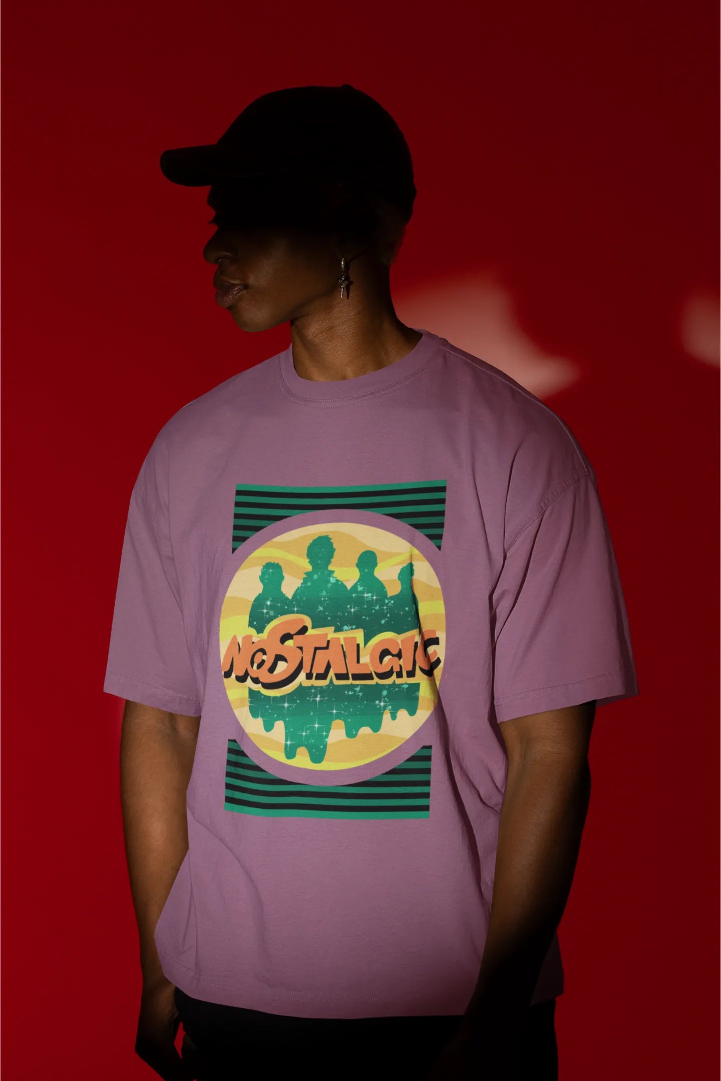 First view of a male model wearing an oversized dirty purple t-shirt with a shadow silhouette of the Coldplay band members and the word "Nostalgic" printed on it.