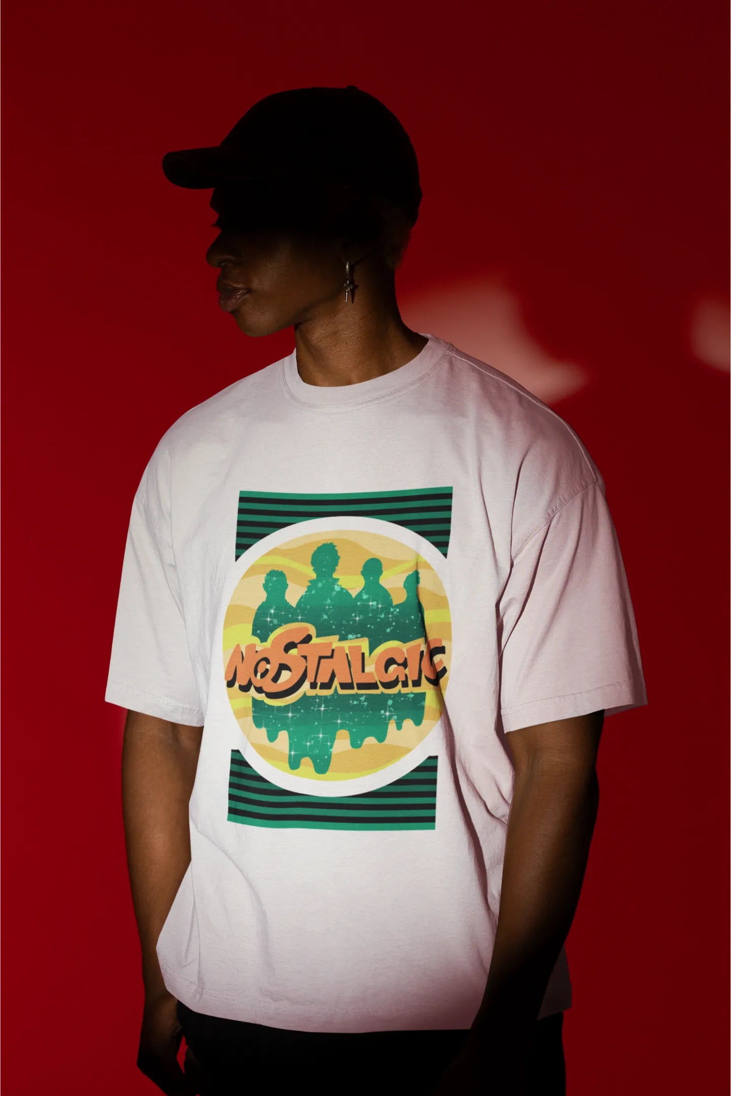 First view of a male model wearing an oversized off-white t-shirt with a shadow silhouette of the Coldplay band members and the word "Nostalgic" printed on it.