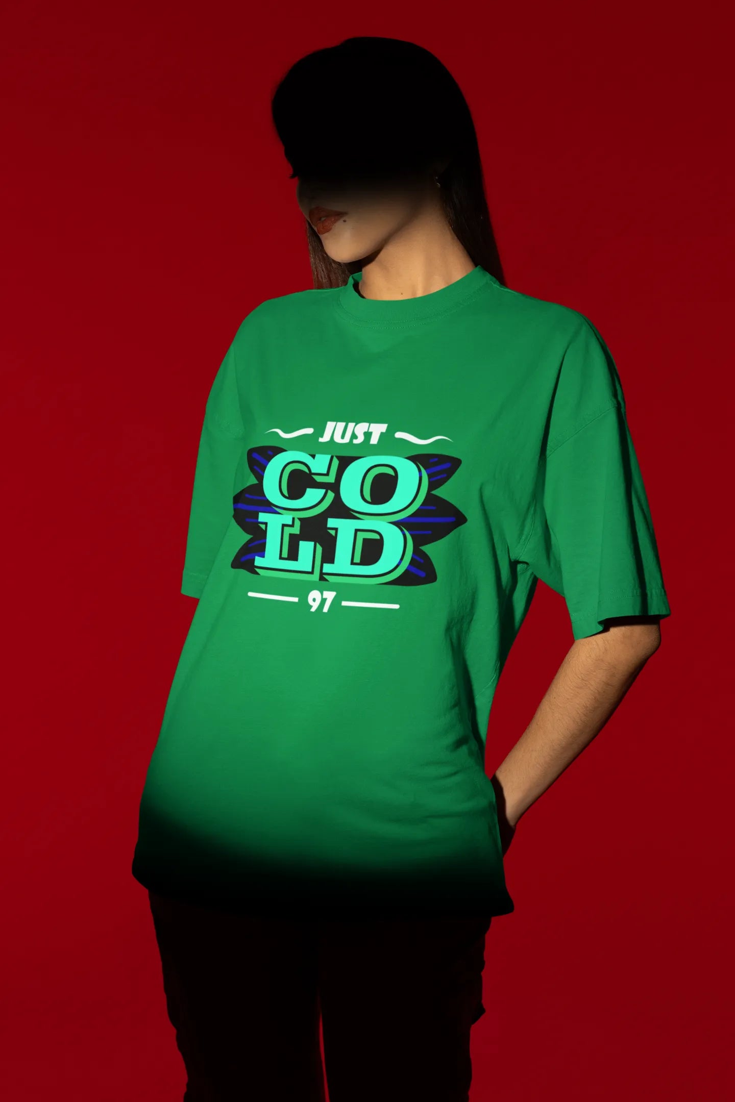 First front view of a female model wearing an forest green oversized t-shirt with the text "Just Cold" printed on it.