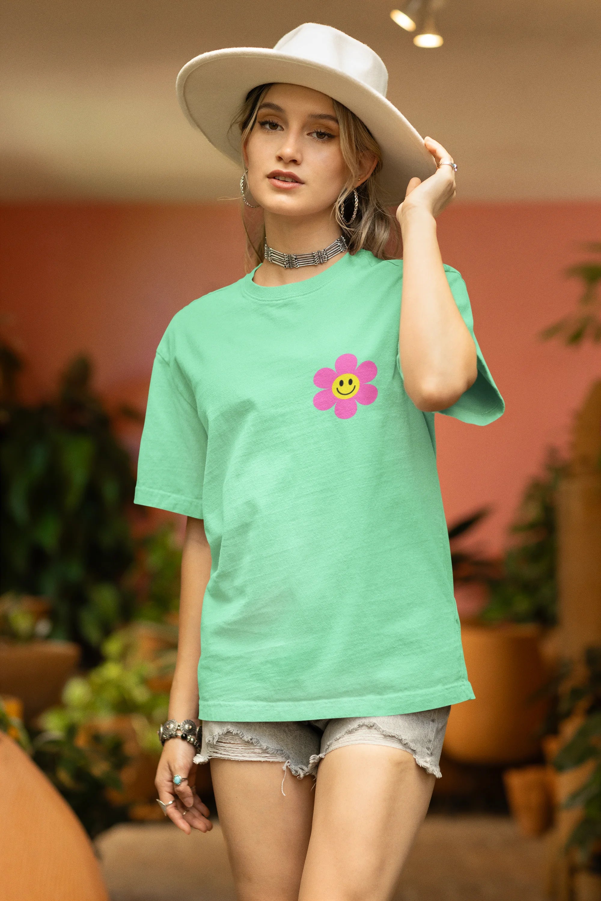 Side view of a female model wearing an oversized mint green t-shirt with a positive message "Keep Smiling" surrounded by colorful flowers and a smiley face emoji. Ideal for those who love cheerful clothing and spreading positivity.