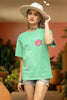 Side view of a female model wearing an oversized mint green t-shirt with a positive message 