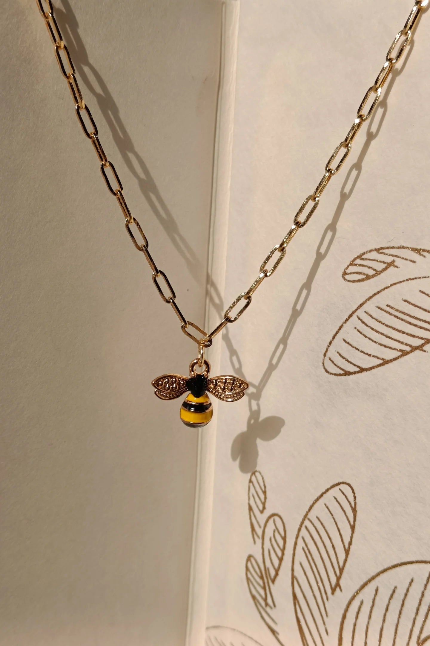 5th view of a gold chain necklace with a small pendant shaped like a honey bee.