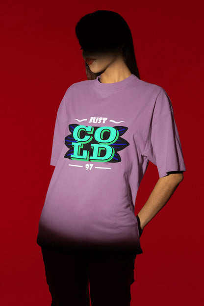 First front view of a female model wearing an dirty purple oversized t-shirt with the text "Just Cold" printed on it.