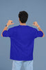 Back view of a male model wearing a royal blue oversized t-shirt with the text 