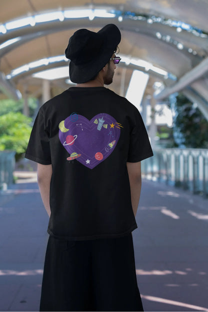 Back view of a male model wearing an black oversized t-shirt with the "Paradise" album artwork by Coldplay.
