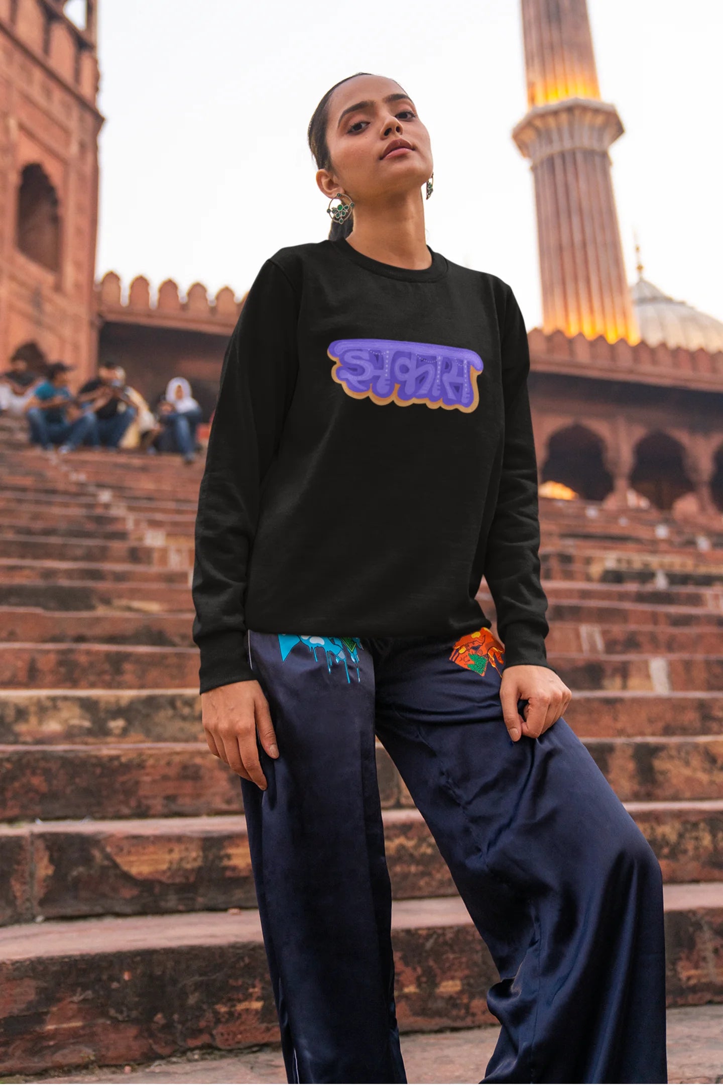 6th front view of a female model wearing an black sweatshirt featuring "Jhakas" in a stylish font.