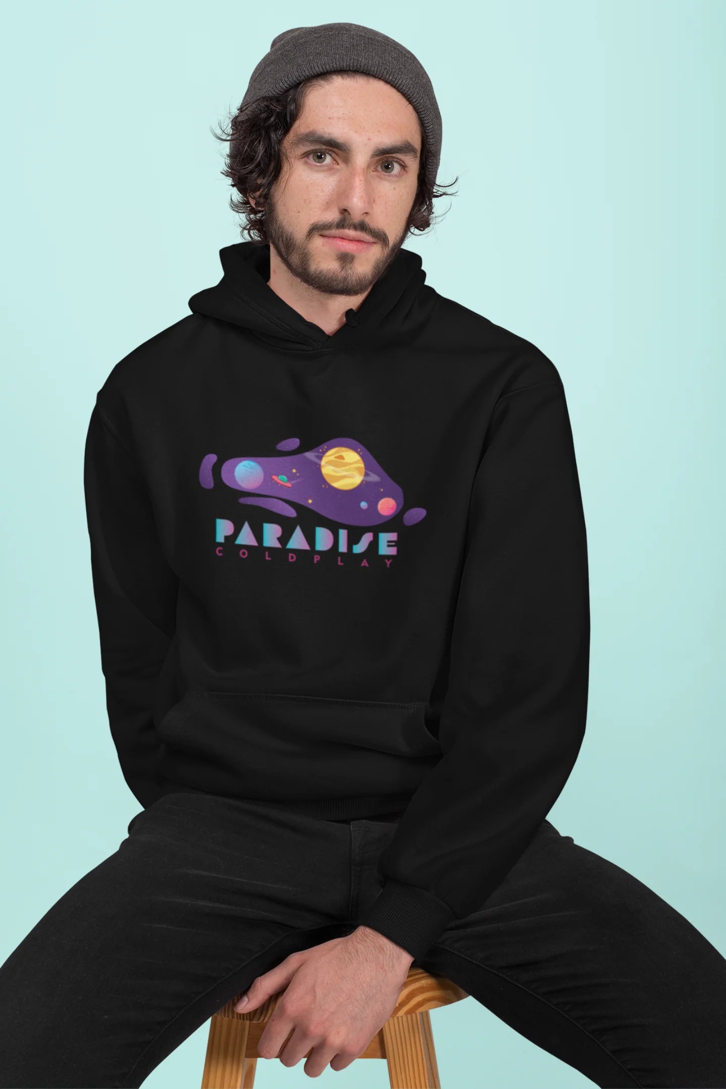 3rd front view of a male model wearing an black hoodie with the "Paradise" album artwork by Coldplay.