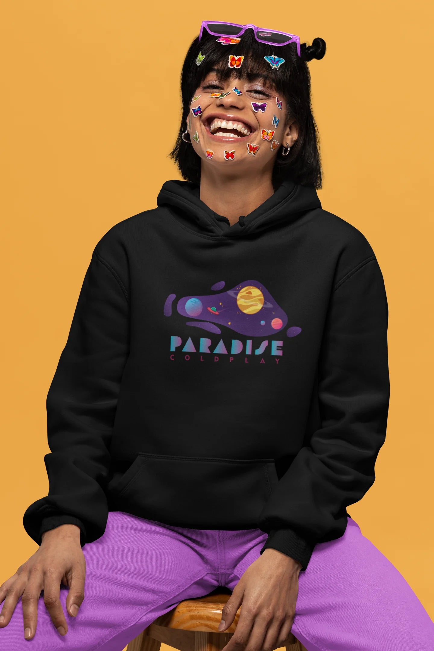3rd front view of a female model wearing an black hoodie with the "Paradise" album artwork by Coldplay.