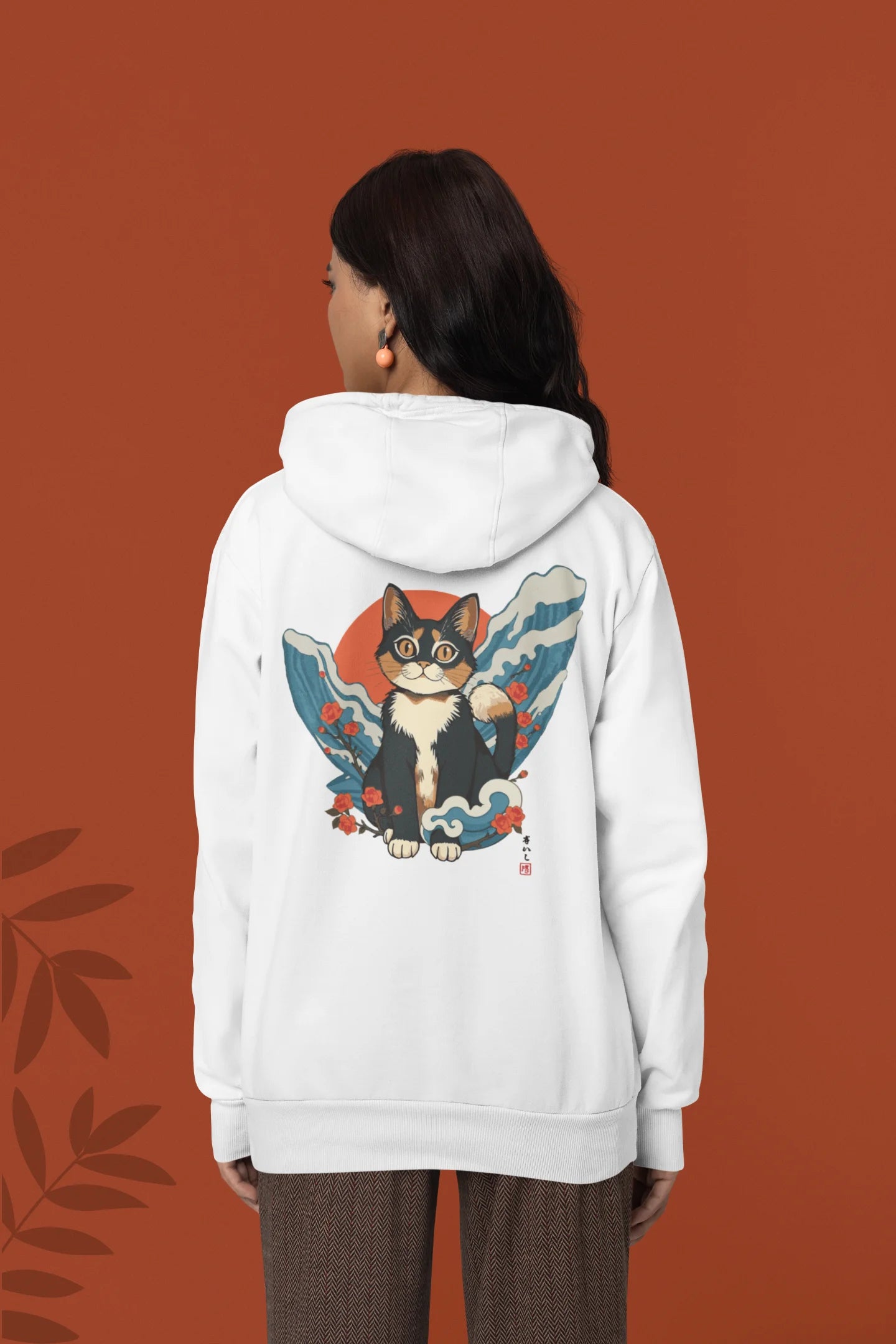 Back view of a female model wearing a white hoodie with a design of a cat dressed as a samurai, standing against a backdrop of waves and a rising sun.