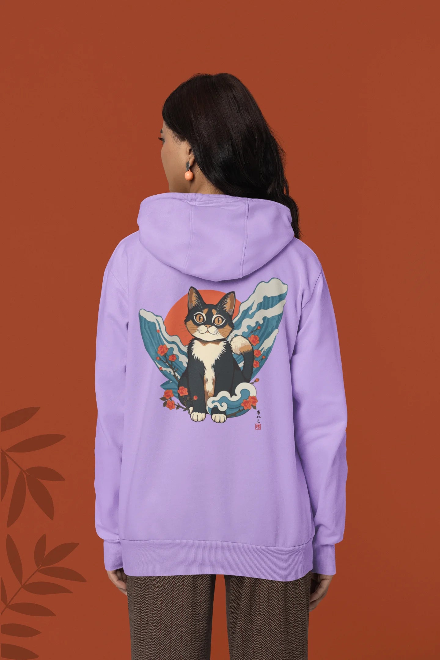 Back view of female model wearing a lavender hoodie with a design of a cat dressed as a samurai, standing against a backdrop of waves and a rising sun.