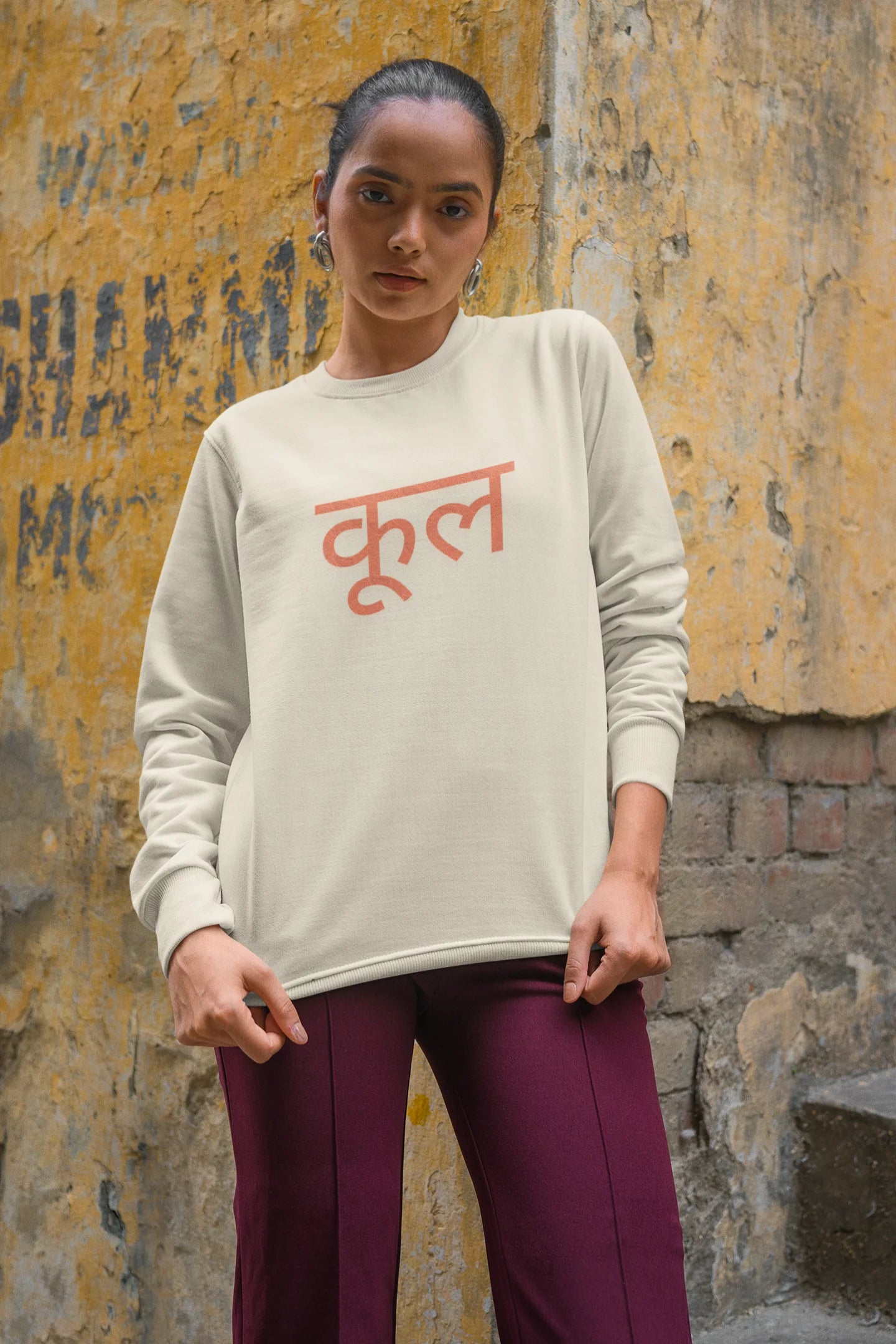 2nd front view of a female model wearing a cream oversized t-shirt featuring the Hindi word for "cool" with a unique, playful design.