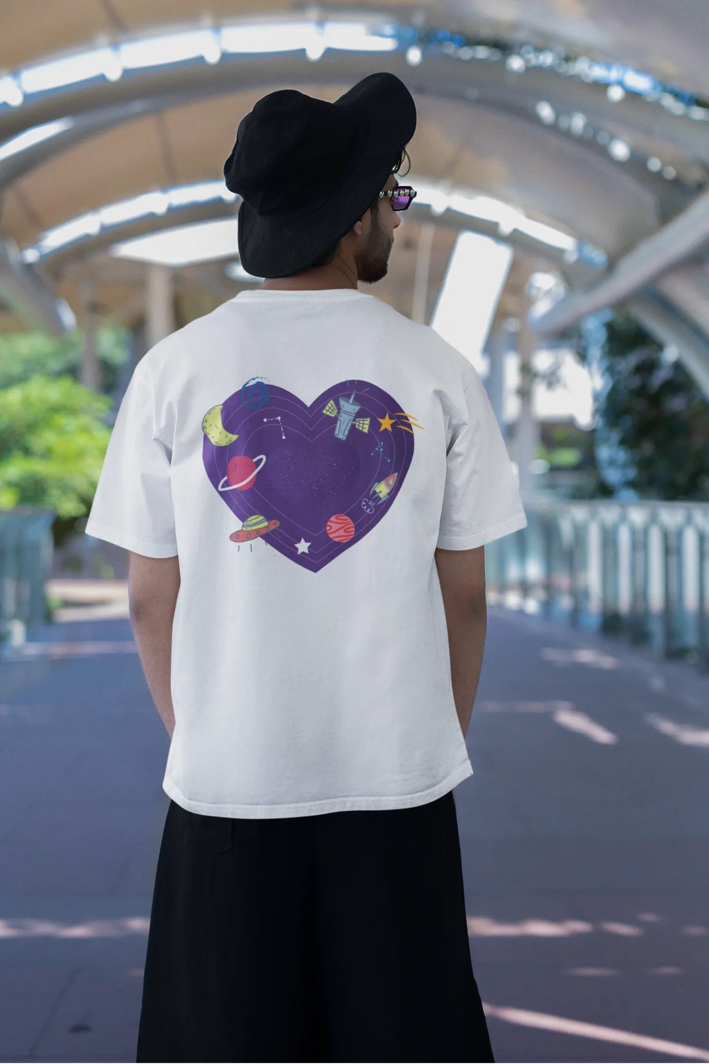 Back view of a male model wearing an white oversized t-shirt with the "Paradise" album artwork by Coldplay.
