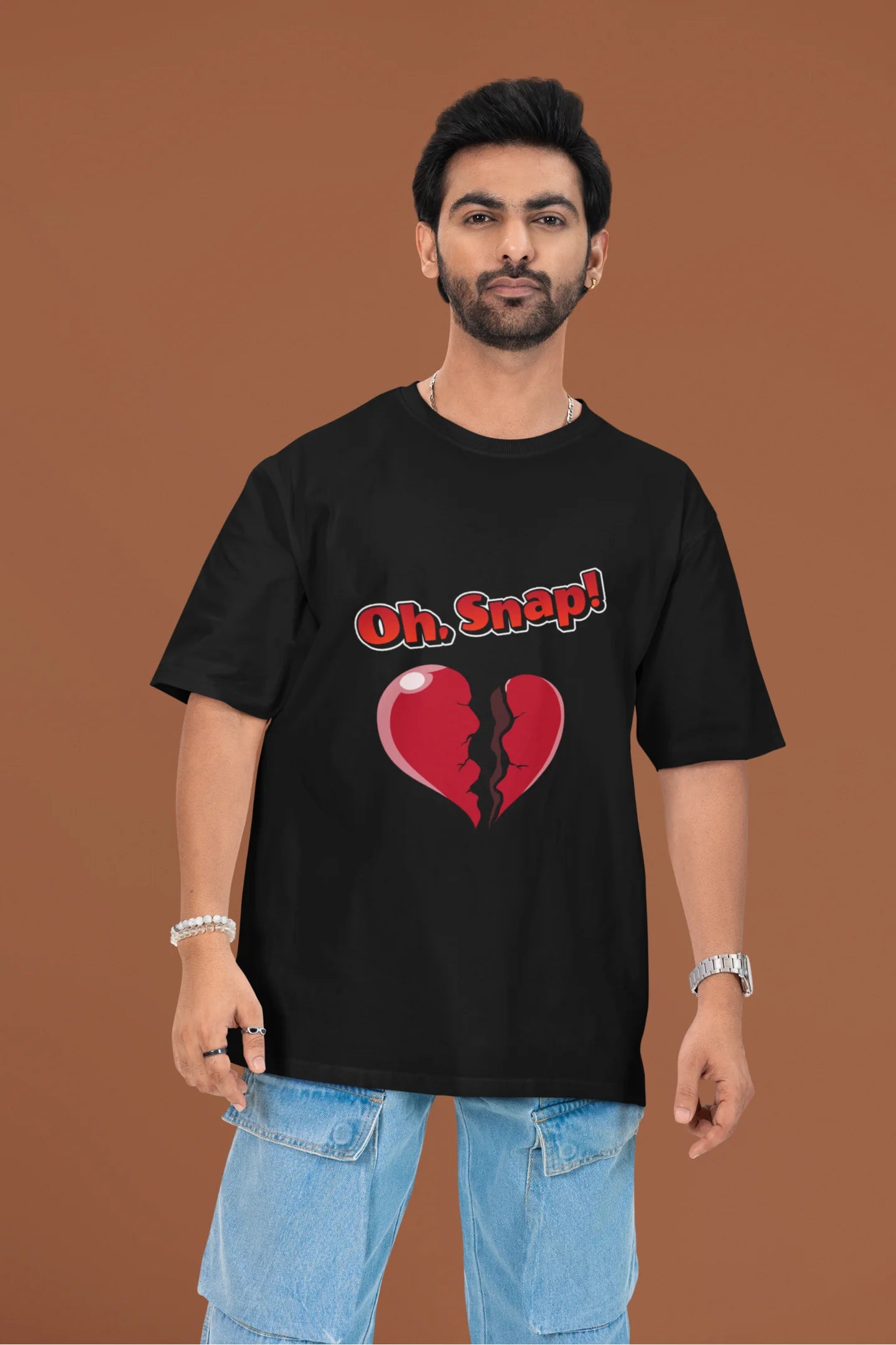 2nd front view of a male model wearing a black oversized t-shirt with the text "Oh Snap!" and a broken heart symbol underneath.