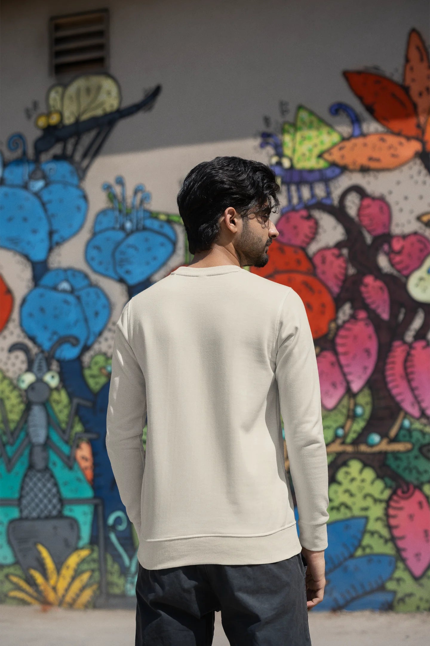 Back view of a male model wearing an cream sweatshirt with a cosmic Universe design inspired by Coldplay.