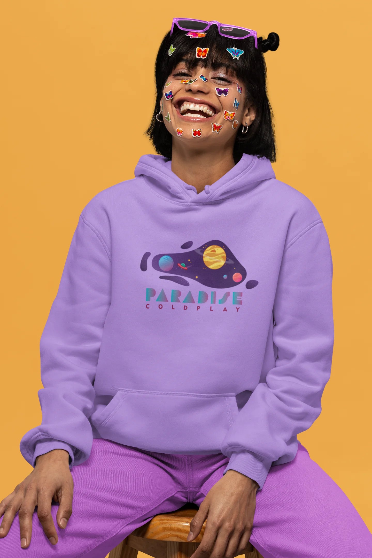 2nd front view of a female model wearing an lavender hoodie with the "Paradise" album artwork by Coldplay.