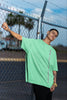 Side view of a male model wearing an mint green oversized t-shirt featuring a thought-provoking design of a man's bust with the text 