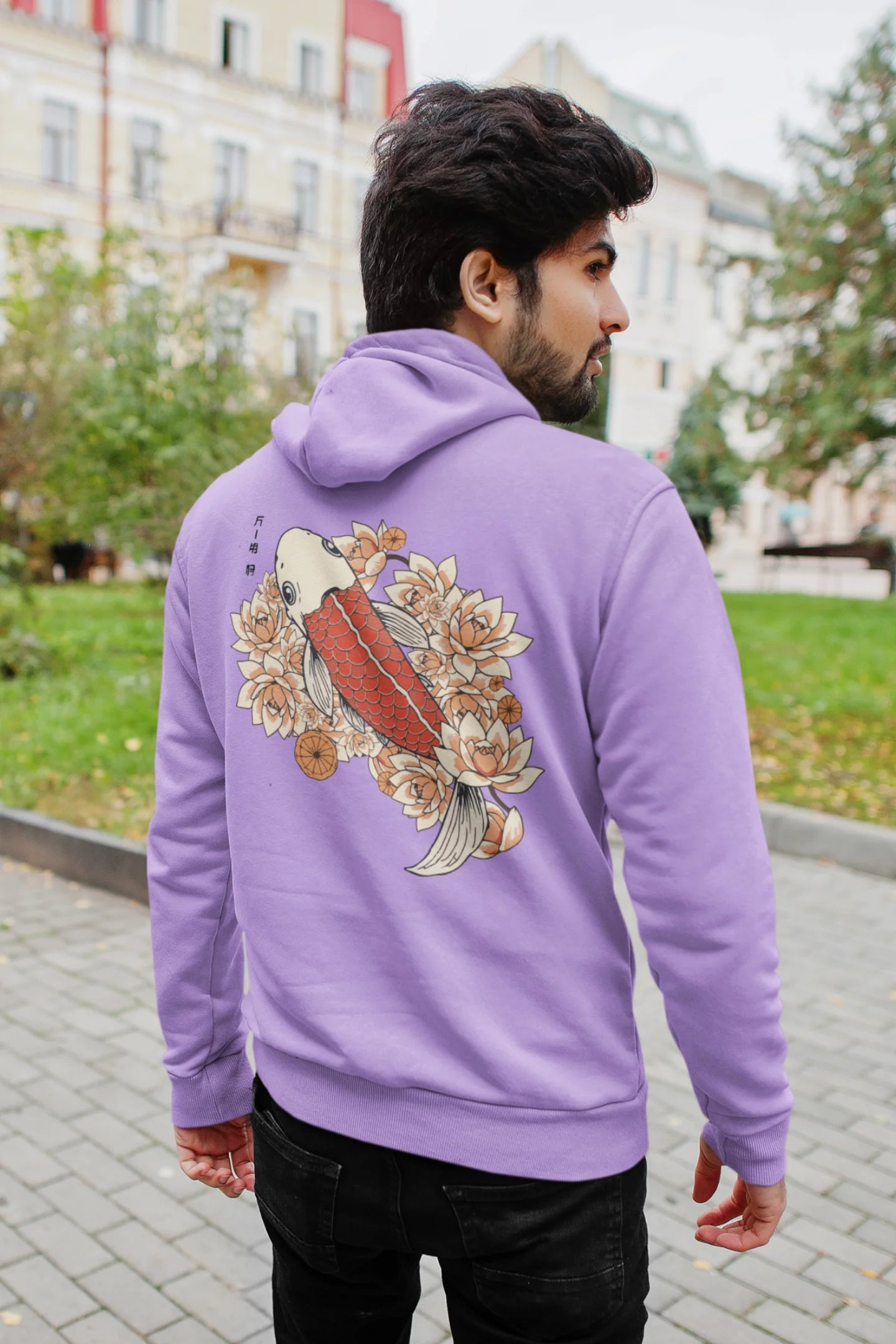 Back view of a male model wearing a lavender hoodie with a design of a koi fish swimming in a bed of flowers.