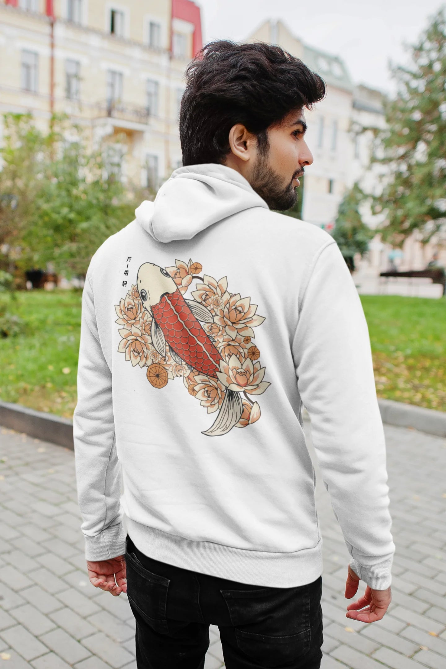 Back view of a male model wearing a white hoodie with a design of a koi fish swimming in a bed of flowers.