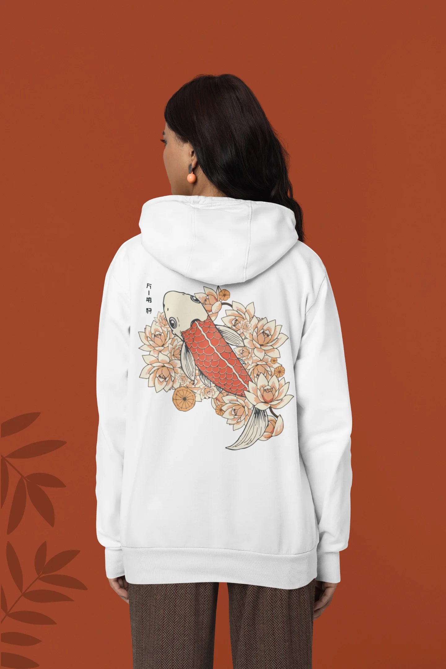 Back view of a female model wearing a white hoodie with a design of a koi fish swimming in a bed of flowers.