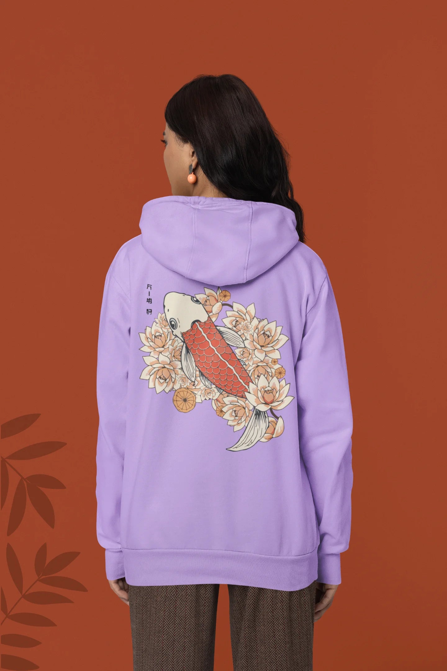 Back view of a female model wearing a lavender hoodie with a design of a koi fish swimming in a bed of flowers.