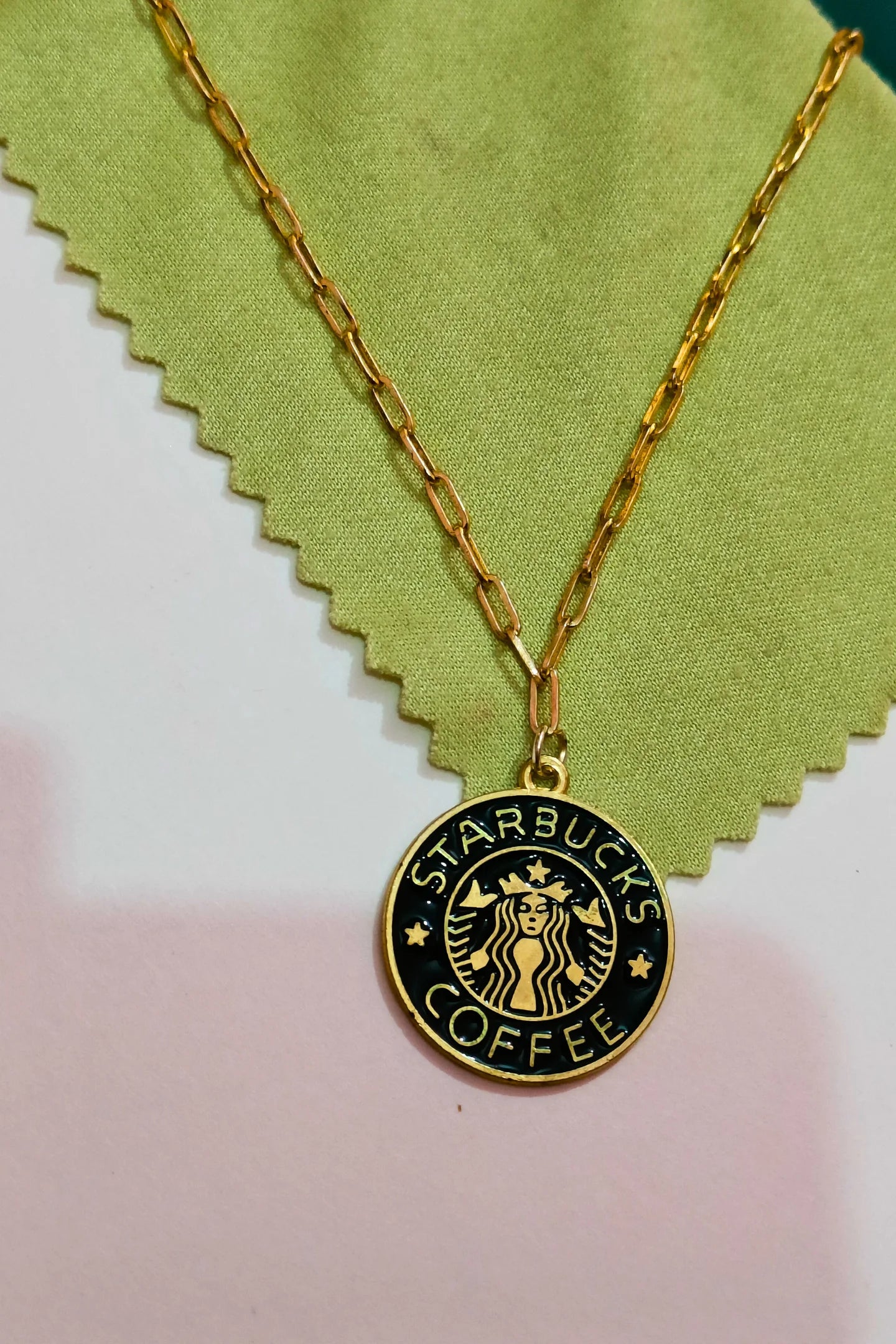First view of a gold chain necklace with a small pendant featuring the Starbucks logo.