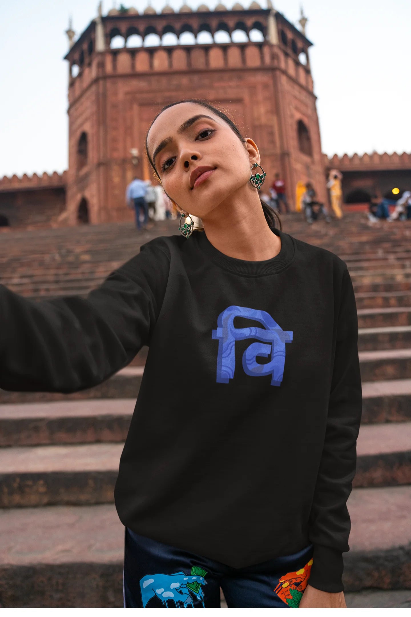 3rd front view of a female model wearing a black sweatshirt with the phrase "Vichitra Pranee" (meaning "Strange being" or "alien") in a stylish Hindi font.