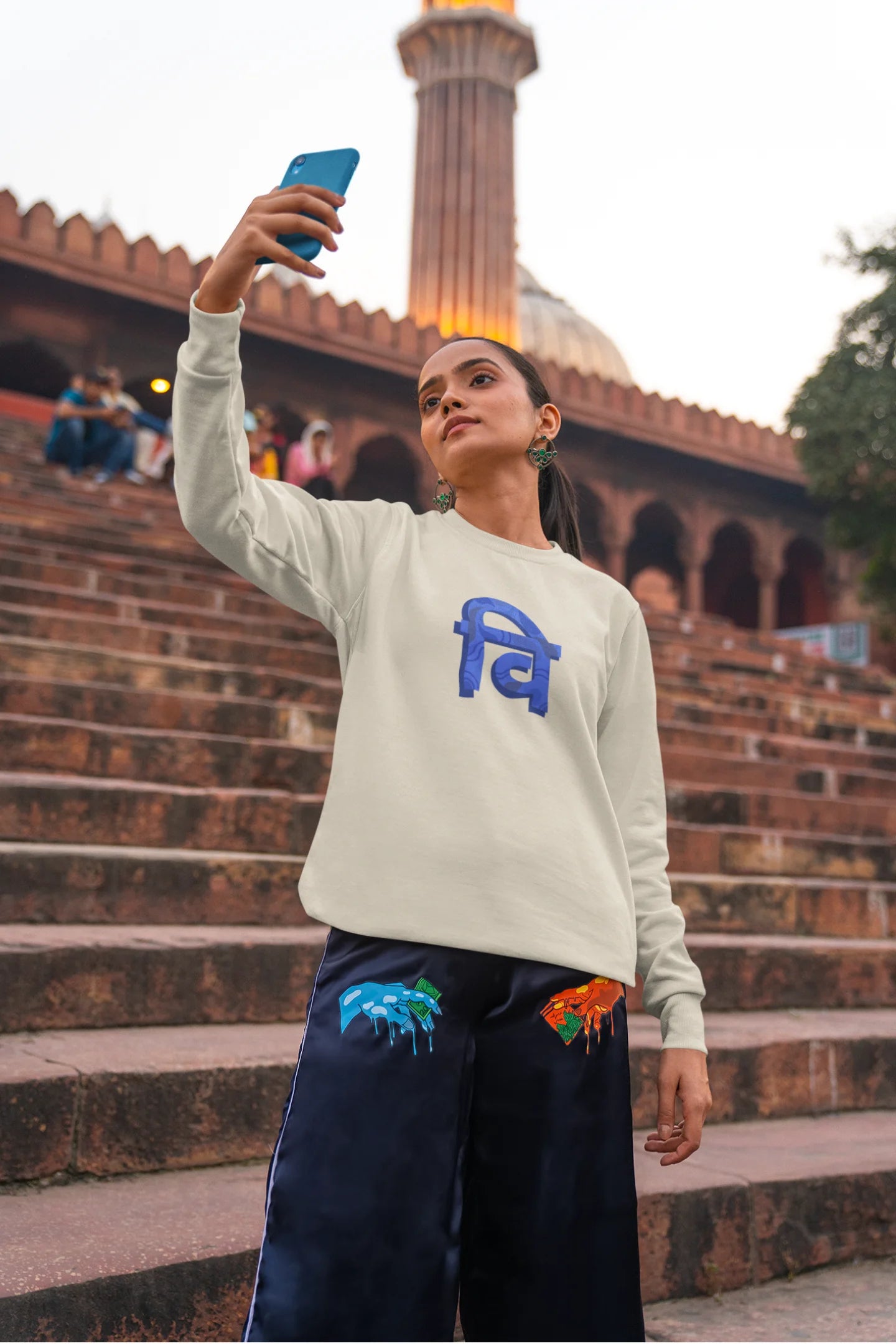 First front view of a female model wearing a cream sweatshirt with the phrase "Vichitra Pranee" (meaning "Strange being" or "alien") in a stylish Hindi font.
