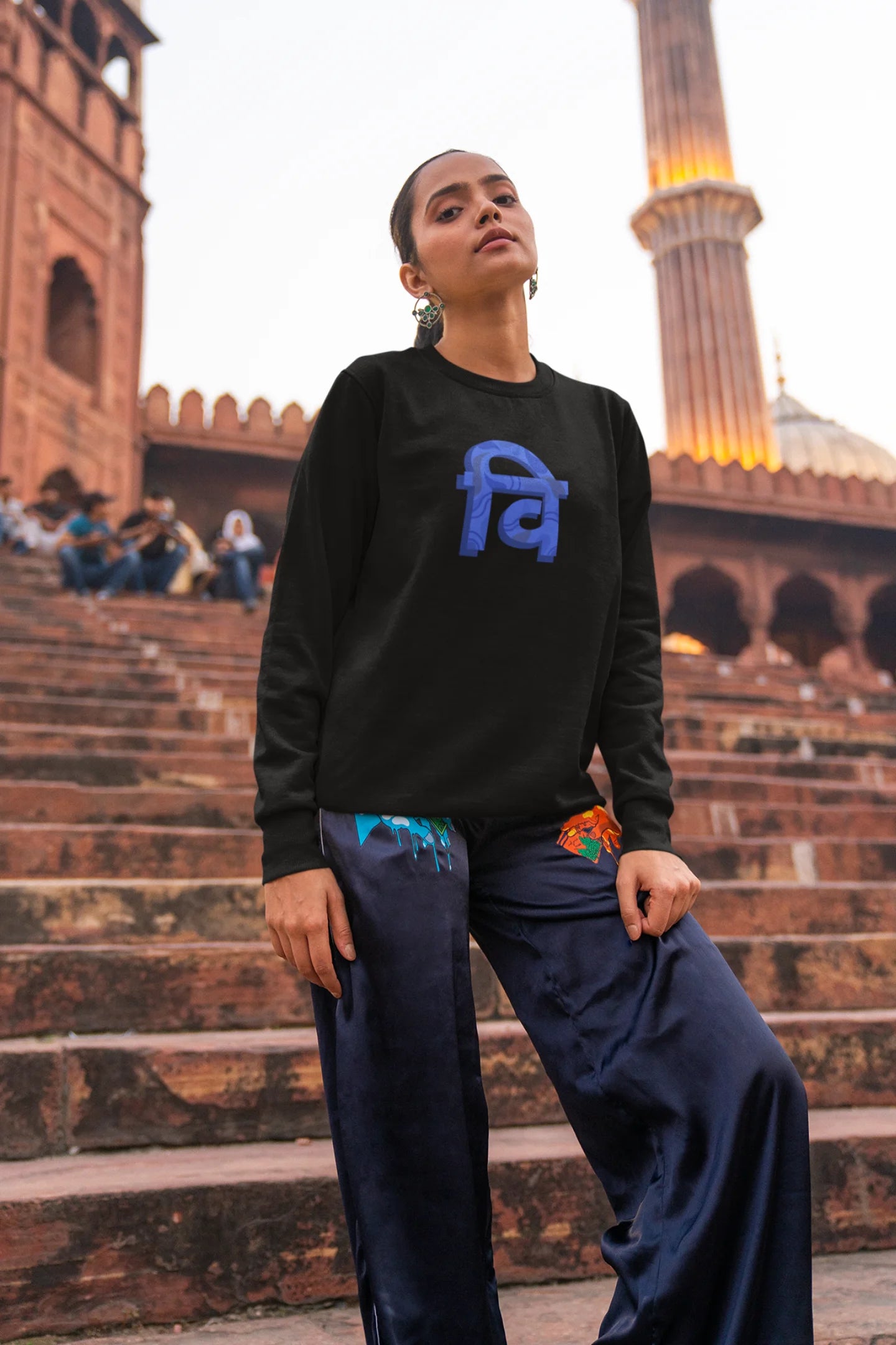 6th front view of a female model wearing a black sweatshirt with the phrase "Vichitra Pranee" (meaning "Strange being" or "alien") in a stylish Hindi font.