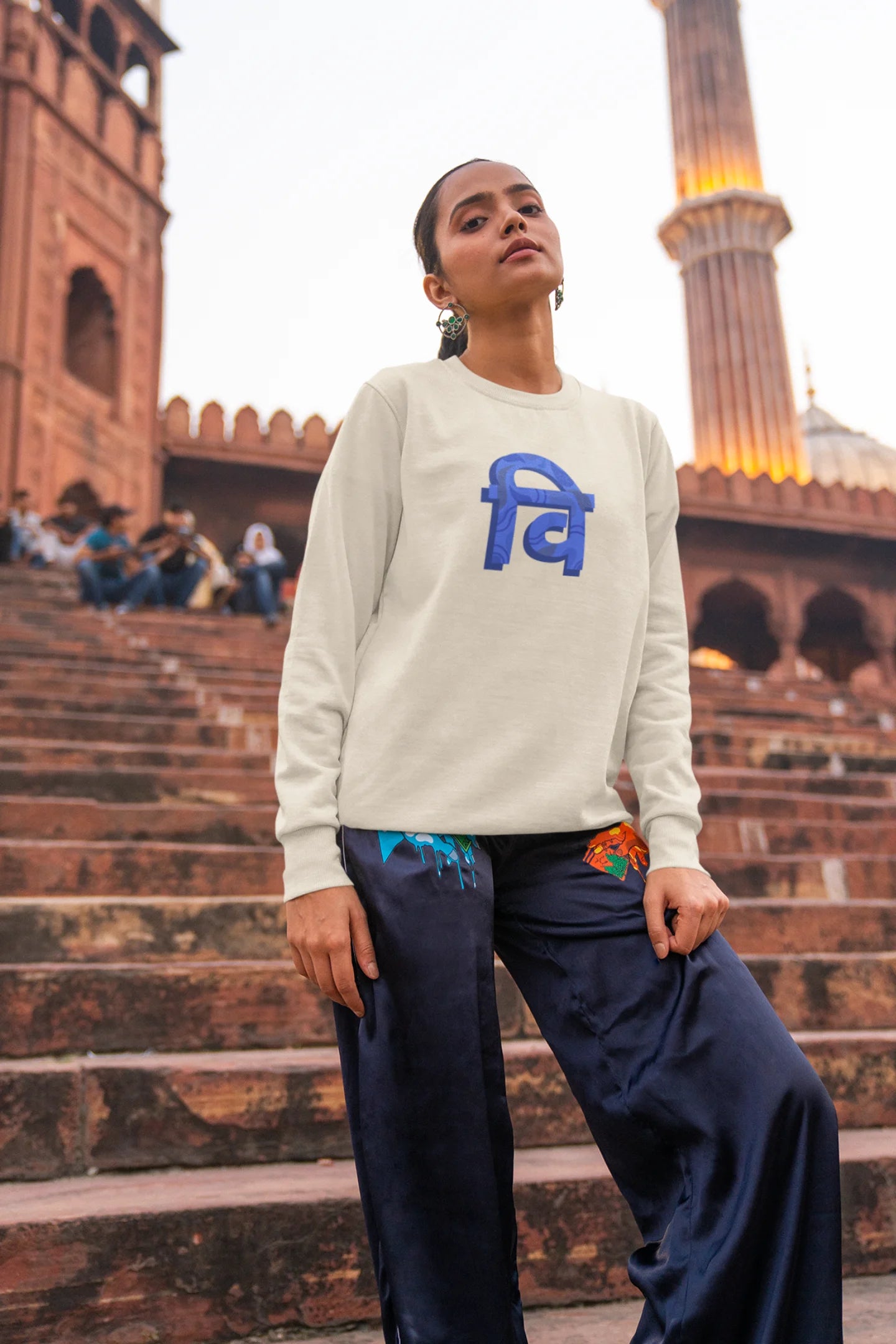 5th front view of a female model wearing a cream sweatshirt with the phrase "Vichitra Pranee" (meaning "Strange being" or "alien") in a stylish Hindi font.