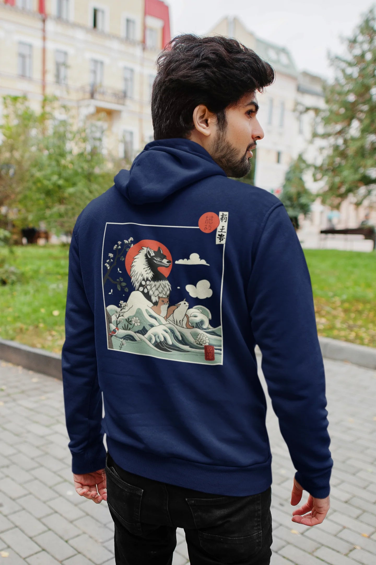 Back view of a male model wearing a navy blue hoodie with a design of a wolf surveying a Japanese landscape.