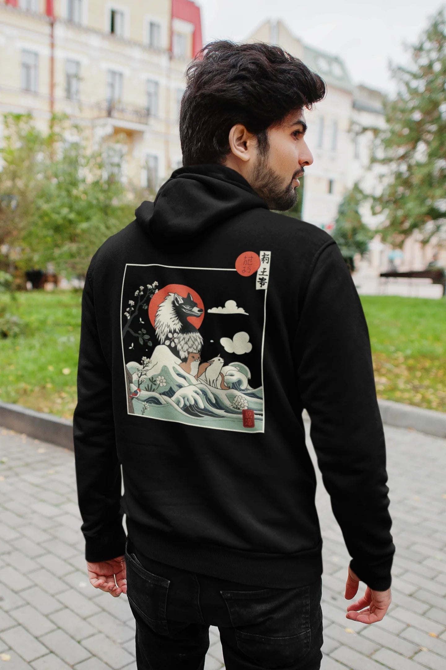 Back view of a male model wearing a black hoodie with a design of a wolf surveying a Japanese landscape.