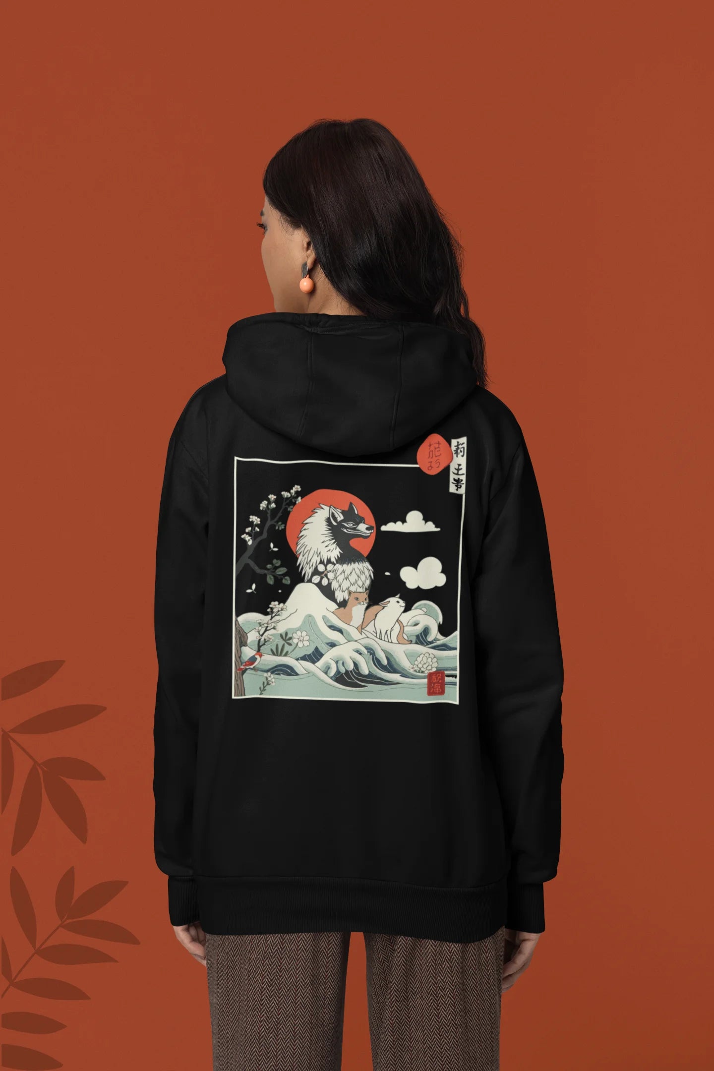 Back view of a female model wearing a black hoodie with a design of a wolf surveying a Japanese landscape.