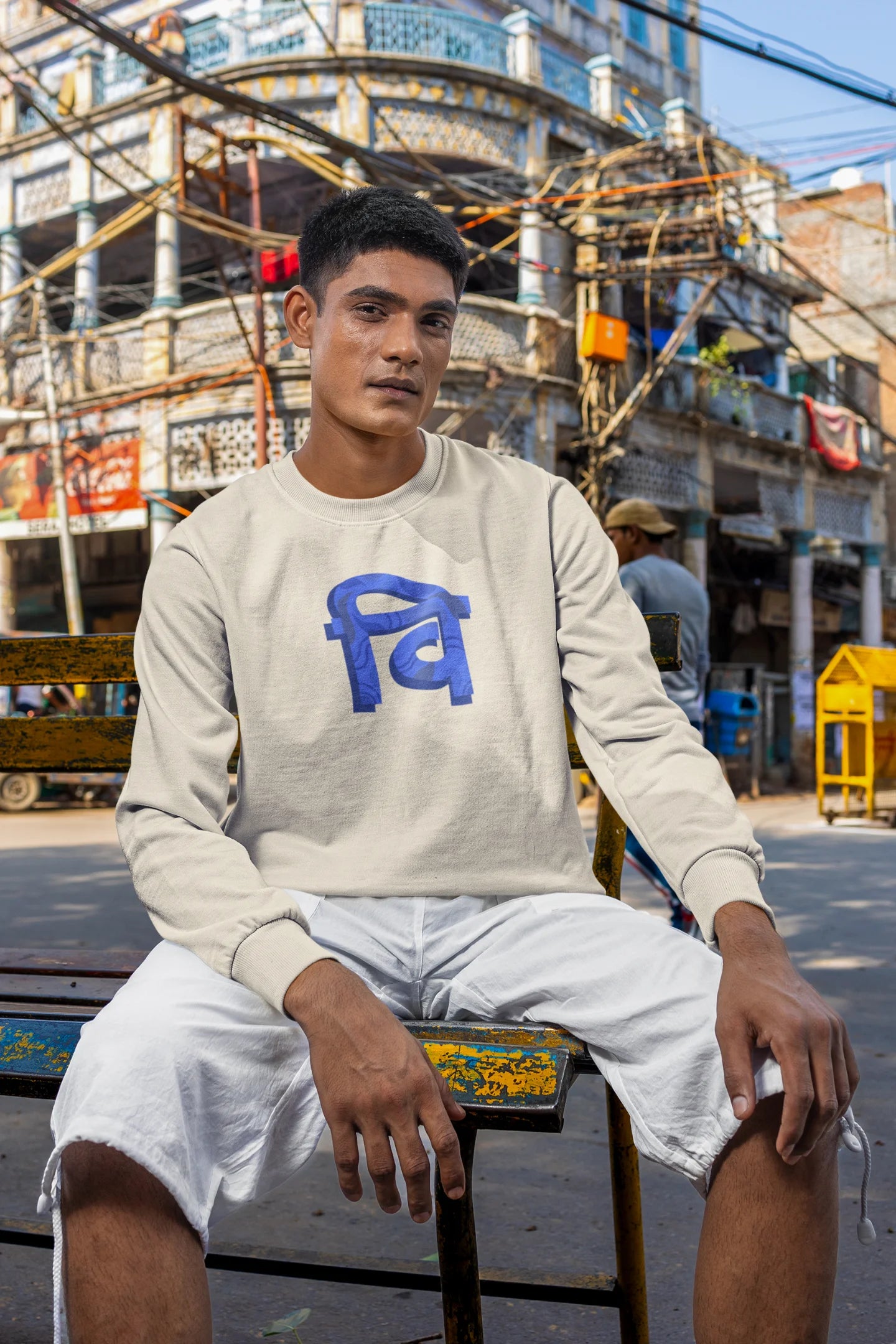 5th front view of a male model wearing a cream sweatshirt with the phrase "Vichitra Pranee" (meaning "Strange being" or "alien") in a stylish Hindi font.