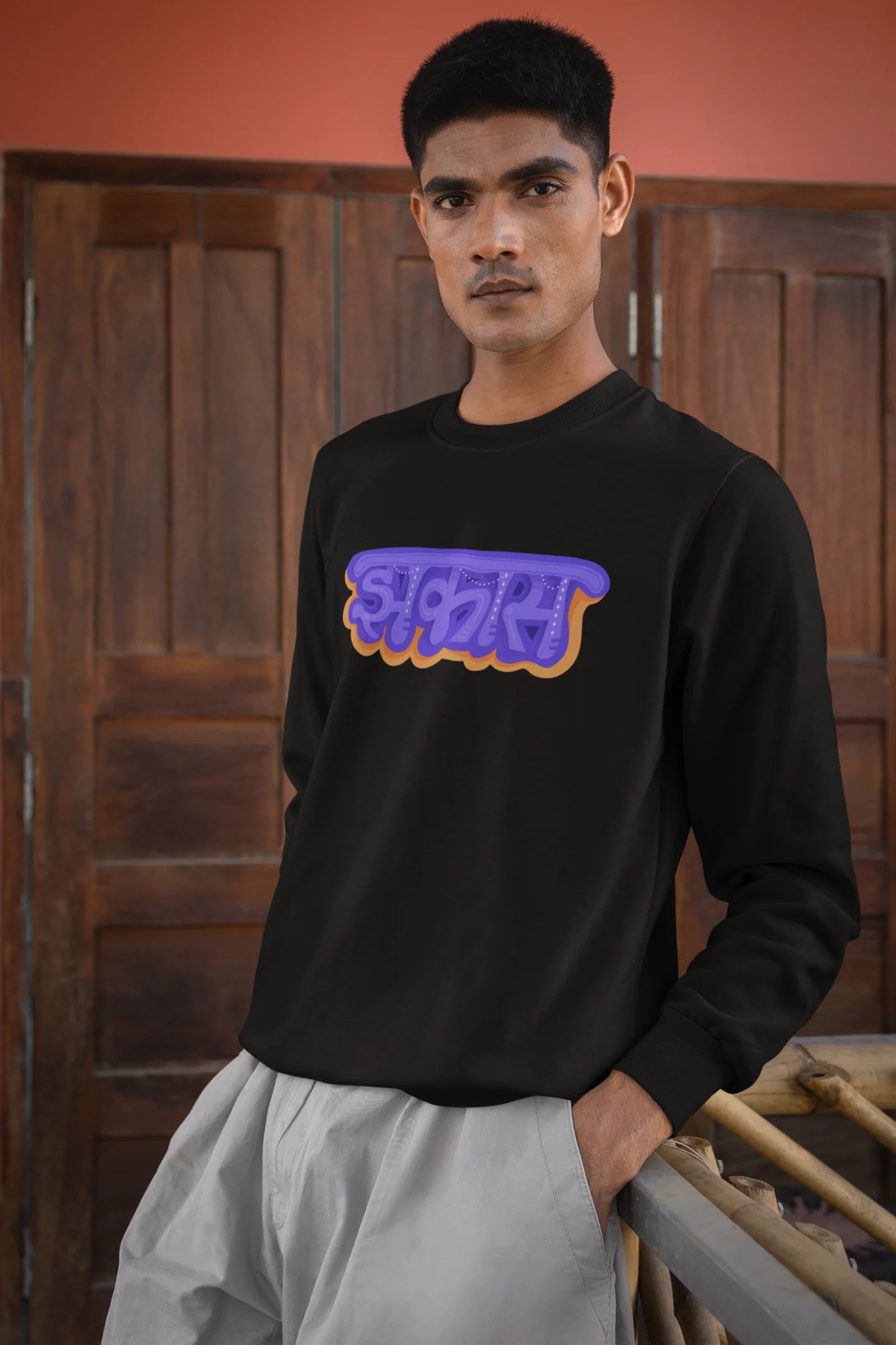 2nd front view of a male model wearing an black sweatshirt featuring "Jhakas" in a stylish font.