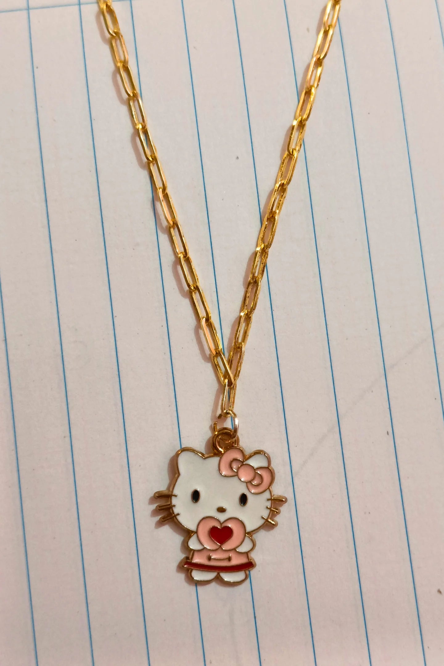 3rd front view of gold chain necklace with a small pendant shaped like Hello Kitty with a heart sign.