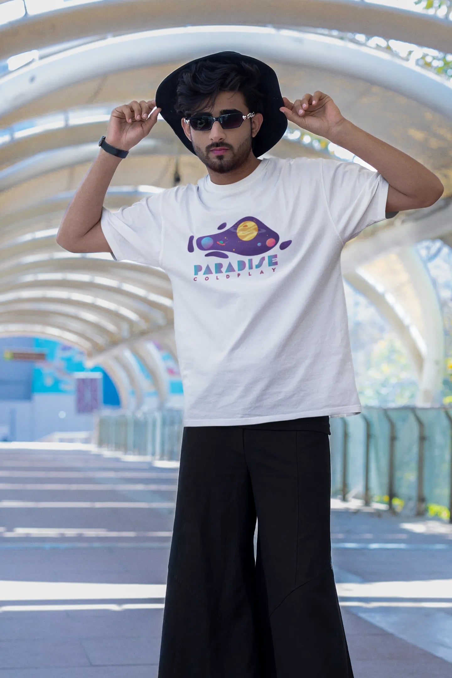 First front view of a male model wearing an white oversized t-shirt with the "Paradise" album artwork by Coldplay.
