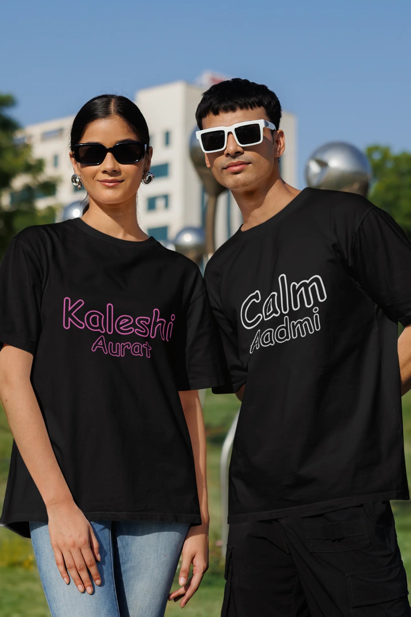 Second front view of a couple wearing matching black oversize tees, one with "Calm one" and the other with "Chaotic one" printed on them in Hindi.