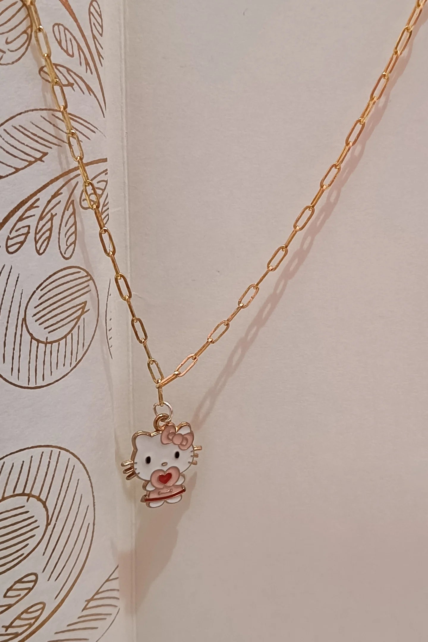 2nd front view of gold chain necklace with a small pendant shaped like Hello Kitty with a heart sign.