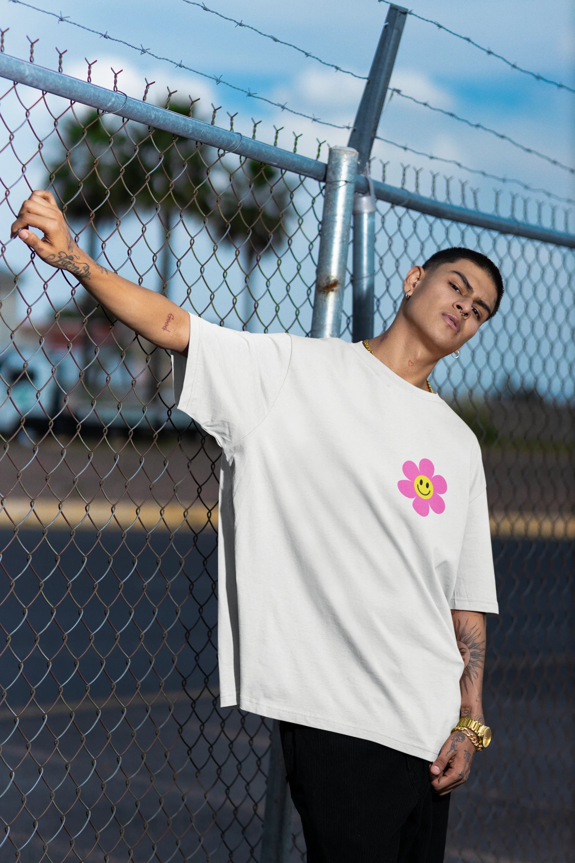 Left side view of a male model wearing an oversized off-white t-shirt with a positive message "Keep Smiling" surrounded by colorful flowers and a smiley face emoji. Ideal for those who love cheerful clothing and spreading positivity.