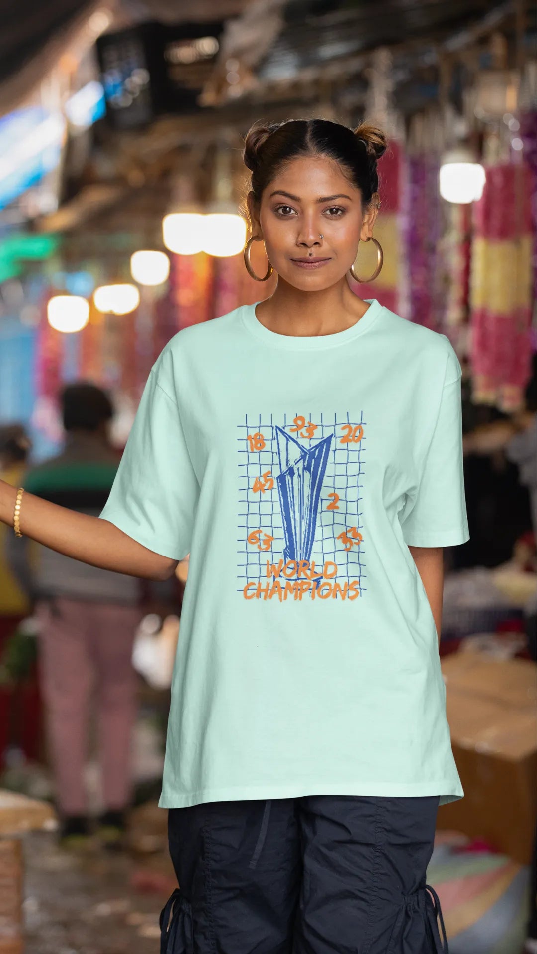 Third front image of female model wearing a mint green oversized t-shirt featuring the World Cup 2024 trophy with the text "World Champions" underneath. Ideal for Indian cricket fans celebrating their team's victory.