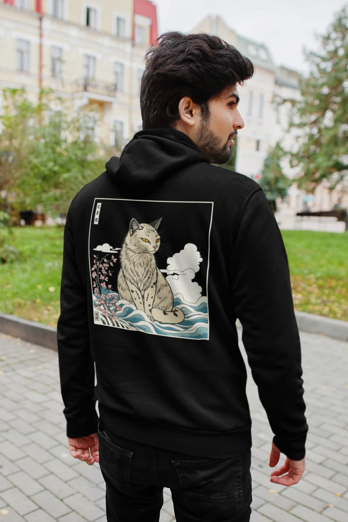 Back view of a male model wearing a black hoodie with a design of a wildcat sitting on ocean waves.
